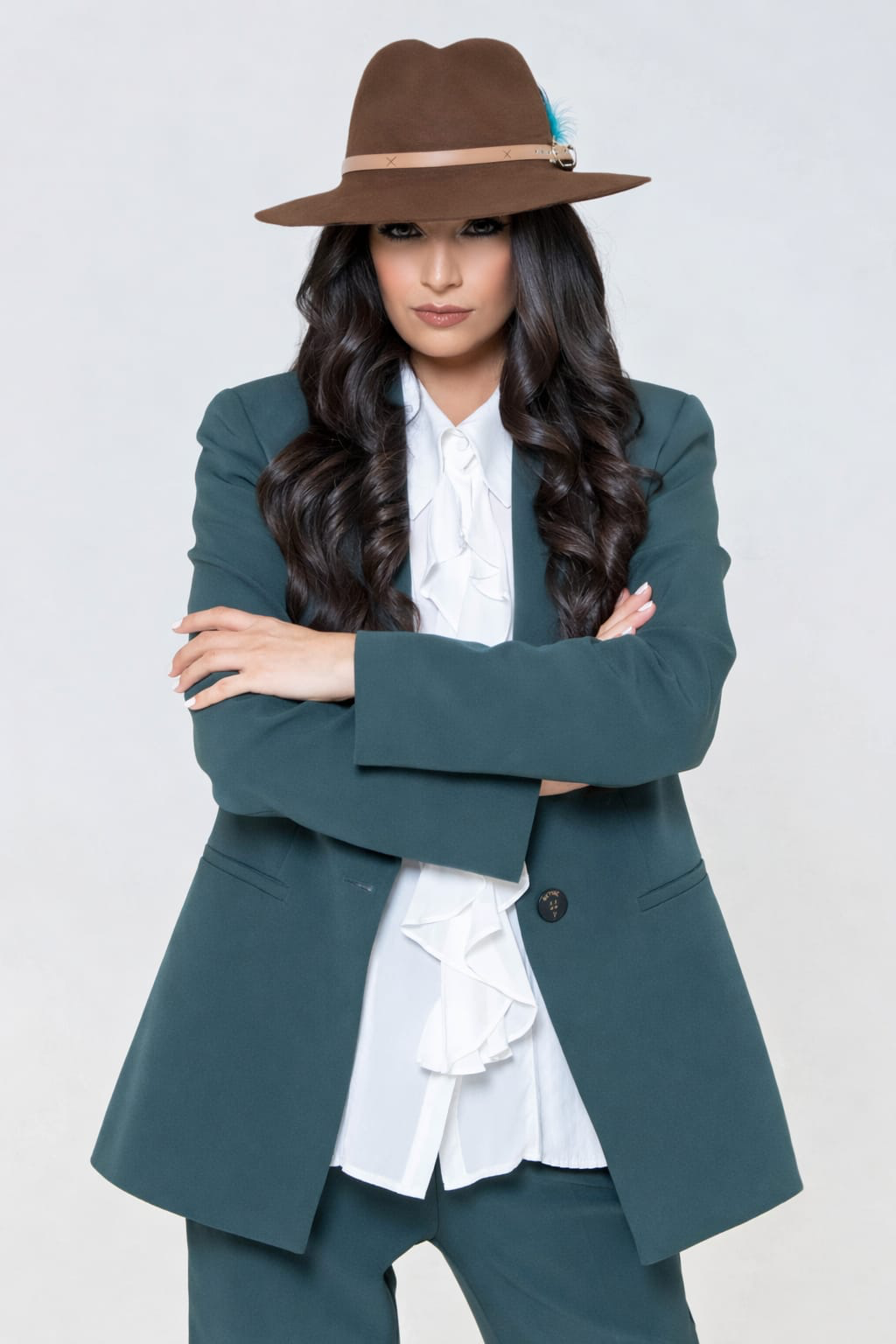 Ghazaleh Ghasemi arms crossed in teal suit and brown fedora, poised Persian-Canadian master of ceremonies editorial portrait